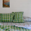 Green plaid pillows on a bed with a scenic poster on the wall.