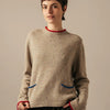 Person wearing a beige sweater with red trim on a plain background