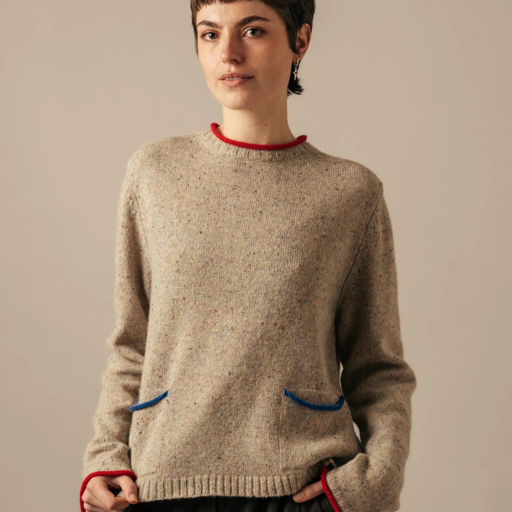 Person wearing a beige sweater with red trim on a plain background