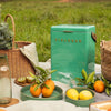 Green 'Fieldbar' cooler with picnic setup including fruits and baskets in a field.
