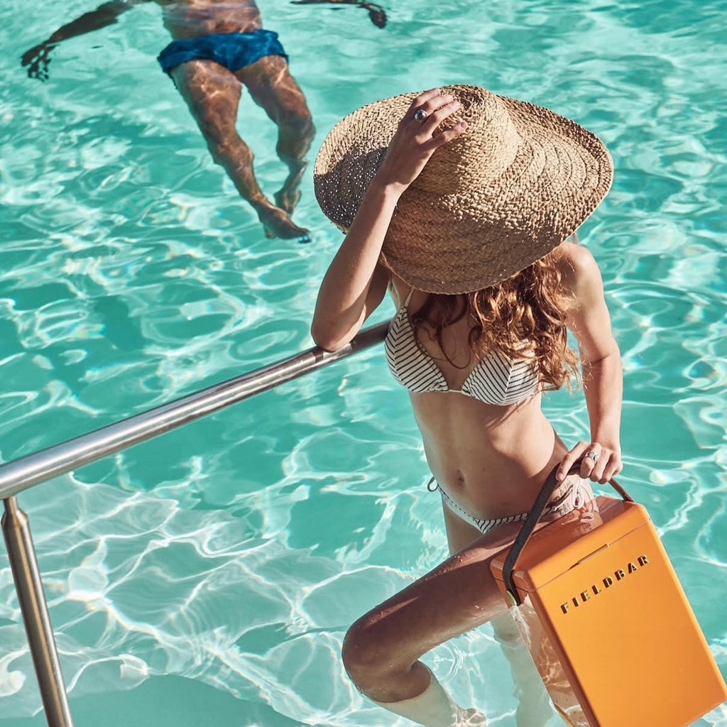 Woman in a pool holding a cooler with a man partially submerged in the water.