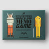 A rectangular printed game box or cover titled "The Movie Memo Game" by Printworks, shown on a light gray background. The front has a teal background with illustrated film-related figures: a person wrapped in bandages on the left, a yellow jumpsuit on the right, and black title text in the center.