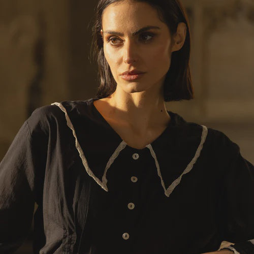 Woman wearing a black blouse with white trim and beige pants in a warm-toned setting