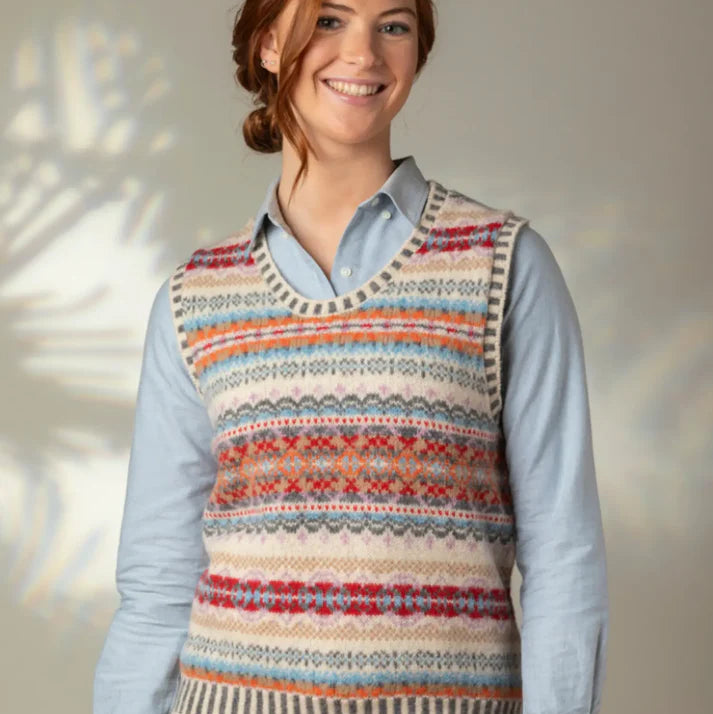 Woman wearing a colorful patterned Eribe vest over a light blue shirt against a neutral background